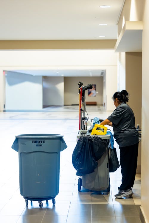 Professional janitorial worker pushing a cleaning cart through a commercial building hallway