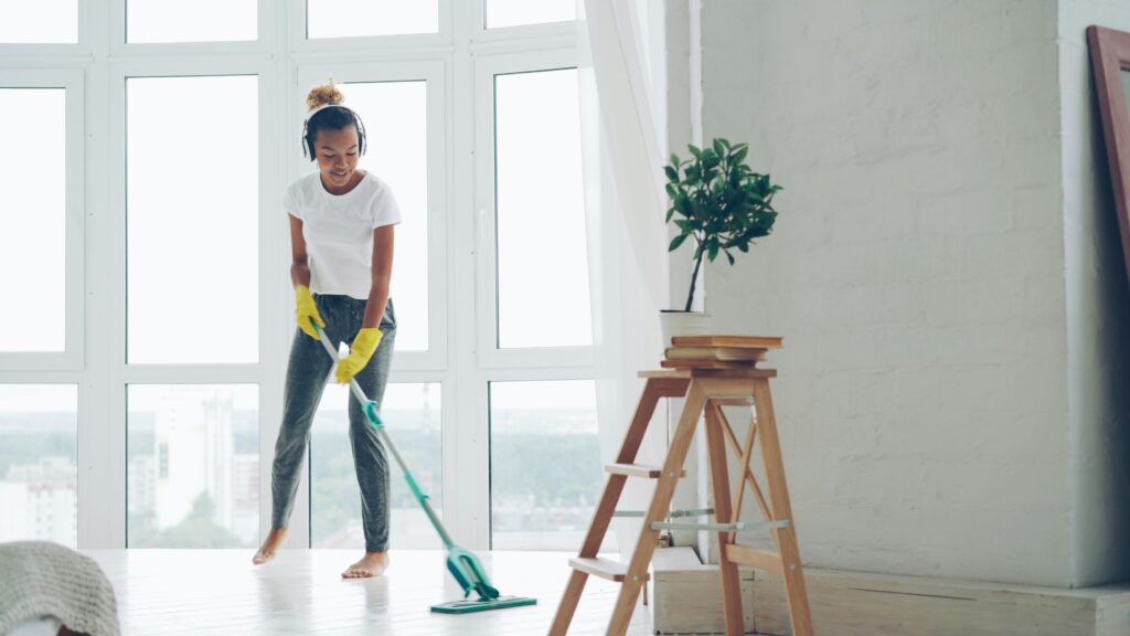 Professional cleaner mopping hardwood floor with green mop near window