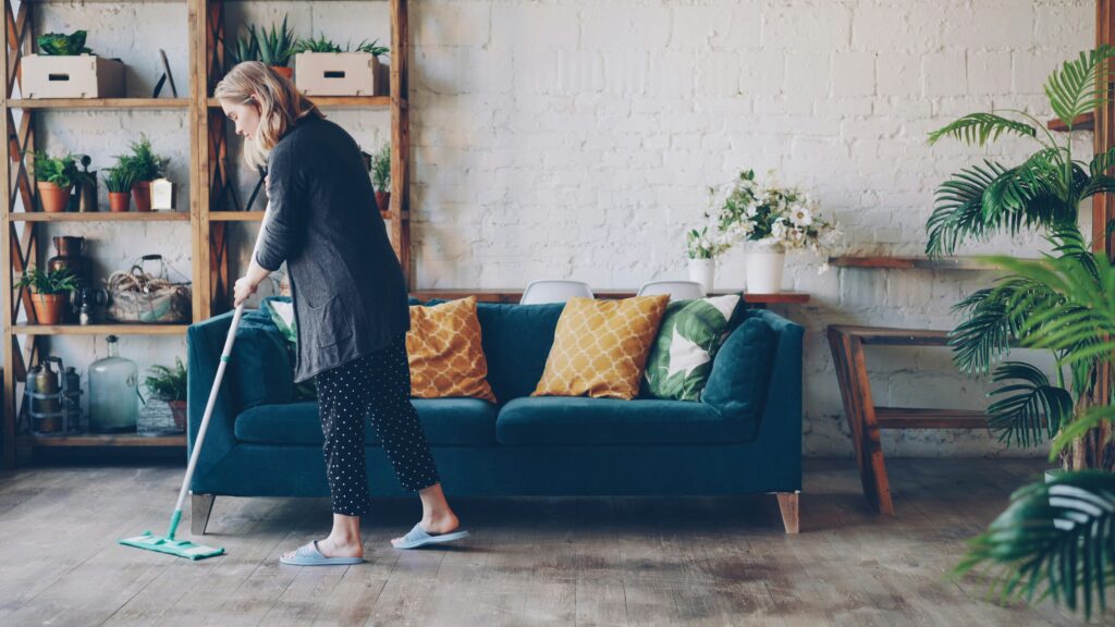 Woman tidying living room and arranging fresh flowers near sofa