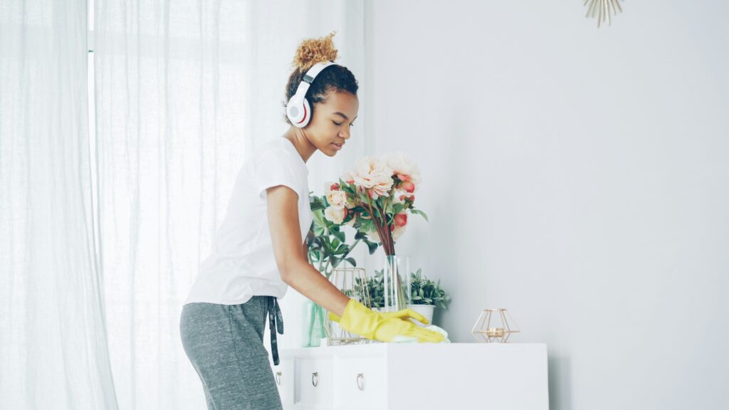 Woman wearing headphones mopping hardwood floor in bright living room